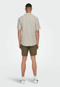 Camisa de manga corta, de color gris claro, con botones y cuello, combinada con pantalones cortos verde oliva y zapatillas blancas, vista desde atrás.