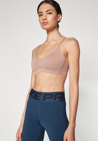 Lys brun sports-BH med tynne stropper, med scoop hals og subtile sømmer. Kombinert med mørkeblå høytlivs leggings med "NIKE PRO" på livbåndet.