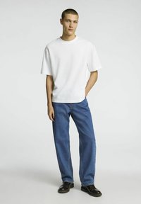 Vit bomulls t-shirt med kort ärm, tillsammans med lösa blå denimjeans. Modellen bär svarta läderskor. Enkel, avslappnad outfitt.
