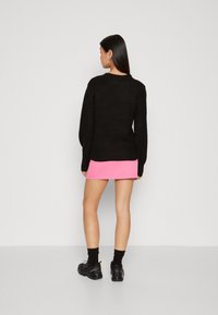 Schwarzer Strickpullover mit langen Ärmeln, kombiniert mit einem rosa Minirock und schwarzen sportlichen Schuhen, von hinten gezeigt.