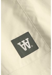 Beige Stoff mit einer glatten Textur, der ein dunkelgrünes rechteckiges Feld mit einem weißen Logo aufweist, das in der Ecke platziert ist.