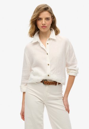 Witte linnen overhemd met een kraag, voorzien van gouden knopen en opgerolde mouwen. Draagt het met lichtgekleurde broek en een bruin geweven riem.