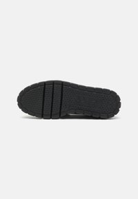 Black rubber shoe sole with textured grip pattern, featuring three segmented sections and branding. Durable construction designed for traction.