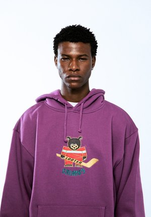 Purple hoodie featuring a bear graphic with a hockey stick and striped jersey. Soft texture, adjustable drawstring, and front pocket.