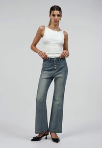 High-waisted, wide-leg denim jeans in light blue. Features five buttons at the front and subtle stitching. Paired with a fitted white tank top.