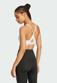 Sujetador deportivo blanco con tirantes entrelazados y un detalle de corte en la parte posterior, combinado con leggings negros de tiro alto. Textura suave.