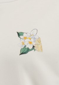 Vit tyg med en broderad design som har gula och vita blommor, gröna blad och en citronskiva på ena sidan.