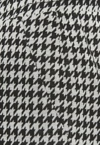 Čierno-biely tkaný vzor houndstooth, textúrovaný úplet s výrazným kostkovaným dizajnom, s jemným leskom a viditeľnými švihmi.