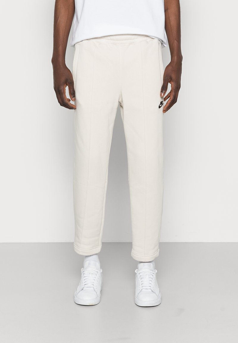 Krämfärgade sweatpants i mjukt tyg, med en avslappnad passform, avslutade ben och en liten svart logotyp på låret, kombinerade med vita sneakers.