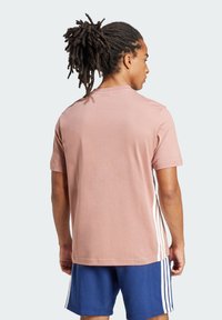 Camiseta de algodón rosa de manga corta con cuello redondo, con rayas blancas a los lados. Textura suave y corte holgado.