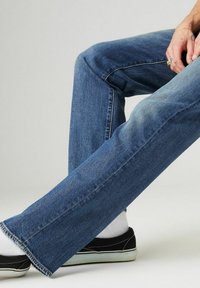 Pantalones vaqueros de mezclilla azul con un diseño de pierna recta, que presentan un ligero desvanecimiento y costuras en contraste, combinados con zapatillas negras y calcetines blancos.