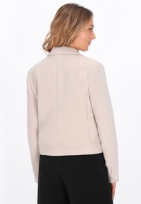 Hellbeige Jacke mit Kragen, tailliertem Schnitt und langen Ärmeln. Hergestellt aus einem weichen Material, mit glatter Textur und minimalistischen Details.