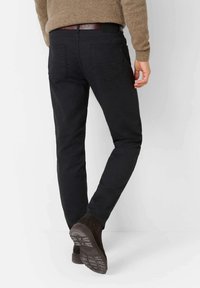 Zwarte slim-fit denim broek met een gemêleerd afwerking, voorzien van twee achterzakken en een bruine leren riem. Gestyled met donkere suede laarzen.