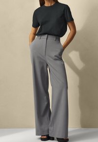 Pantaloni ampi grigi a vita alta, con una texture morbida e dettagli plissettati, abbinati a una t-shirt nera aderente.