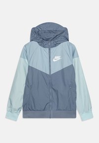 Nike-huppari sinisen eri sävyissä, jossa on vetoketjullinen etuosa, kontrastiväriset hihat, logo rinnassa ja joustavat hihansuut tiukkaa istuvuutta varten.