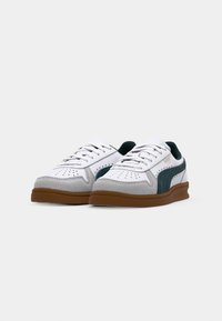 Bílé tenisky s šedými semišovými akcenty, zelenými textilními bočními panely a hnědými gumovými podrážkami. Mají perforované detaily a šněrování.