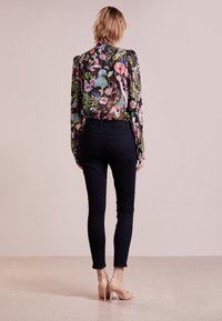 Blusa de flores de manga larga con fondo negro, combinada con jeans oscuros y zapatos de tacón nude, vista desde la parte de atrás.