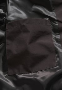 Mustast riidest, sileda tekstuuriga kangas, millel on ruudukujuline tasku. Pind on õrnalt läikiv ja õmblused on tehtud sobiva värvi niidiga.