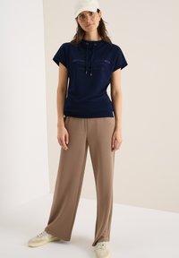 T-shirt à manches courtes navy avec cordon de serrage et texte imprimé, associé à un pantalon large beige et des baskets beiges. Textures lisses et design décontracté.