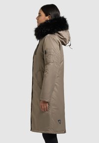 helepruun pikk mantel, millel on musta karvaga kapuuts, küljetaskud ja lukuga varrukatasku; sile tekstuur, loodud soojuse ja kaitse tagamiseks.