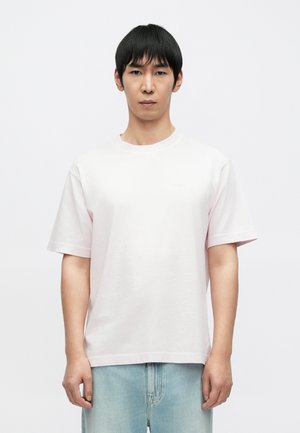 Lyserosa bomulls-T-skjorte med korte ermer, rund hals og en avslappet passform. Har subtil merkevarelogo på brystet. Brukes med lyseblå jeans.