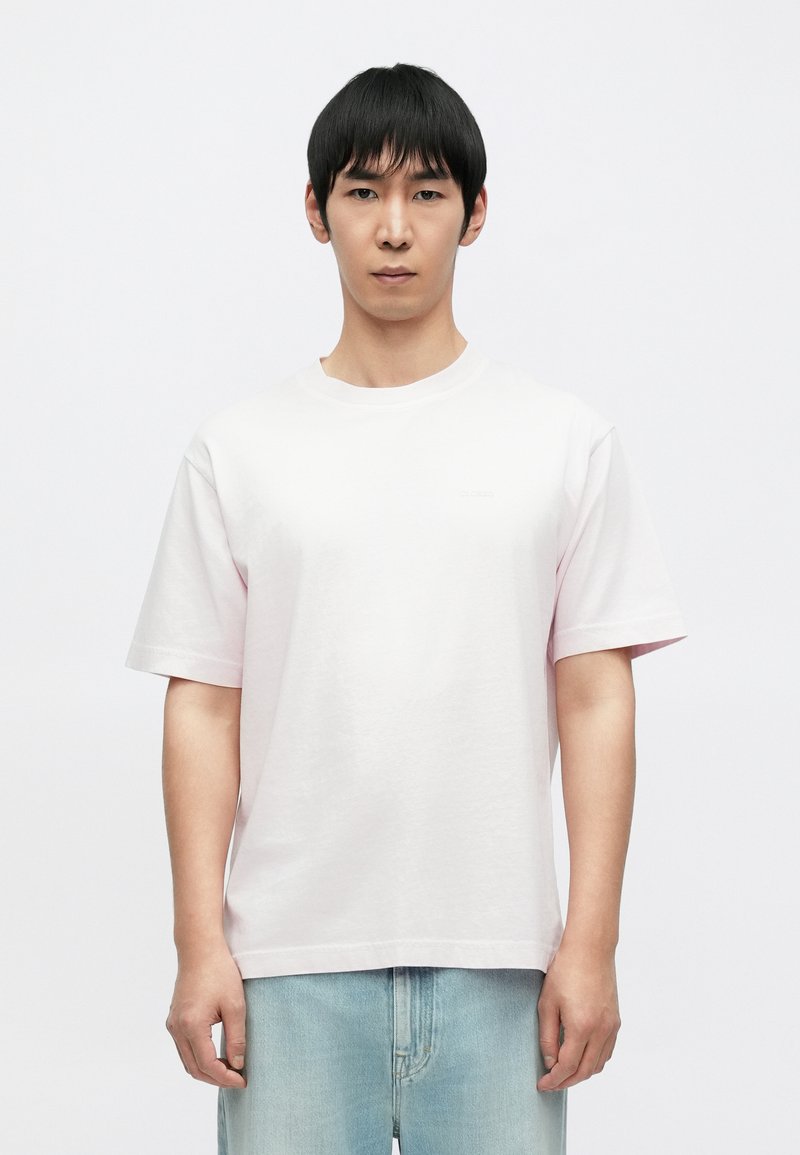 Ροζ βαμβακερό μπλουζάκι με κοντά μανίκια, στρογγυλή λαιμόκοψη και άνετη γραμμή. Έχει διακριτικό λογότυπο στο στήθος. Φοράται με ανοιχτό μπλε τζιν.