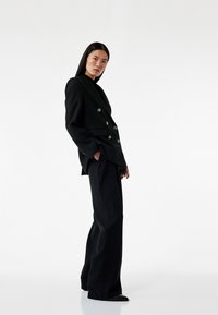 Zwarte dubbelzijdige blazer met zilveren knopen, gecombineerd met hoge zwarte broeken. Soepele textuur, op maat gemaakt pasvorm, minimalistisch ontwerp.