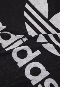 Toalla negra con gran logo blanco de Adidas y tres rayas distintivas, con una tela texturizada para mayor capacidad de absorción.