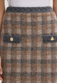 Wollrock mit einem braunen Karomuster und grauen Akzenten. Abgeschlossen mit einem geflochtenen Taillenbund und Knöpfen in goldfarbener Optik an den aufgesetzten Taschen.