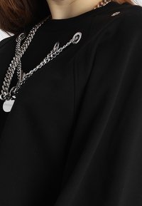 Maglione nero con scollo a girocollo, maniche ampie e dettagli in catena d'argento. Texture liscia con occhielli e etichetta del logo.