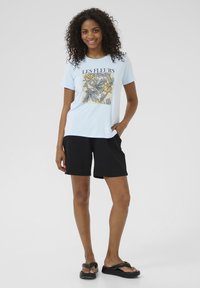 Lichtblauw t-shirt met een bloemenafbeelding en de tekst "LES FLEURS", gecombineerd met zwarte shorts en zwarte slippers, met een relaxte fit.