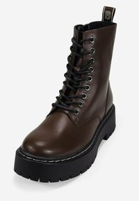Botas de cuero marrón oscuro con cordones, suela de plataforma gruesa negra y tirador en el talón con marca.