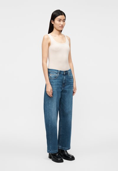 Beige linne, vida blå jeans i denim och svarta klumpiga skor. Har en rundad urringning och en avslappnad passform med raka ben.