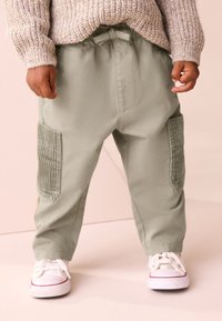 Pantaloni di cotone verde chiaro con vestibilità rilassata, dotati di tasche laterali con texture a coste e vita elastica. Indossati con sneakers bianche.