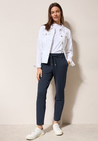 Veste en denim blanc sur un t-shirt blanc uni, associée à un pantalon slim bleu marine et des baskets blanches avec des accents gris.