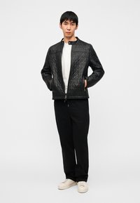 Veste matelassée noire avec col montant et fermeture éclair, présentant un motif géométrique. Associée à un pantalon noir et des baskets blanches.