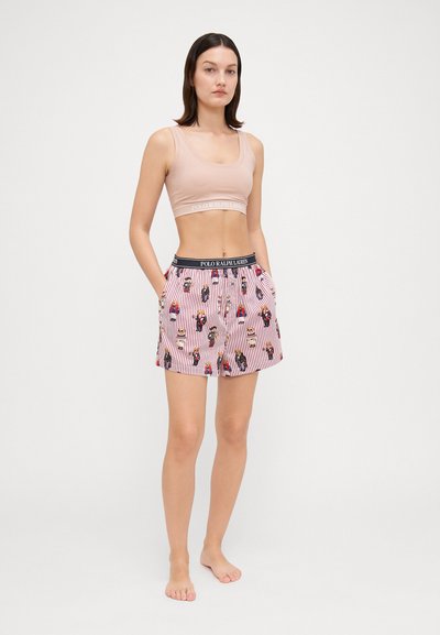 Svetle růžový crop top s pružným pásem a značkovým logem, v kombinaci s šortkami s červenými pruhy, které mají hravé ilustrace a elastický pas.