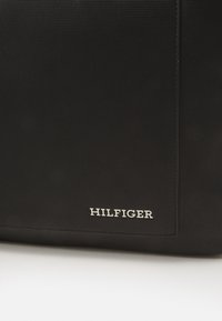 Borsa nera con texture, caratterizzata da un logo "HILFIGER" argentato sul davanti, con linee semplici e dritte e un design elegante.