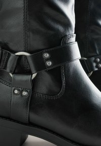 Mustad mustad nahast pahkluu saapad, mis sisaldavad külgrihmaga, millel on metallist rõngas ja hõbedased nupud, siledast tekstuurist ja madalast plokknähtusest.