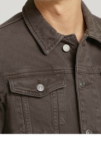 Veste en denim marron avec un col pointu, des boutons pression argentés et des poches poitrine. Présente une surface texturée et des coutures contrastantes.