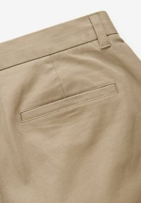 Beige katoenen broek met een gladde textuur, een enkele achterzak en gestikte naden. De tailleband is plat en voorzien van riemlussen.