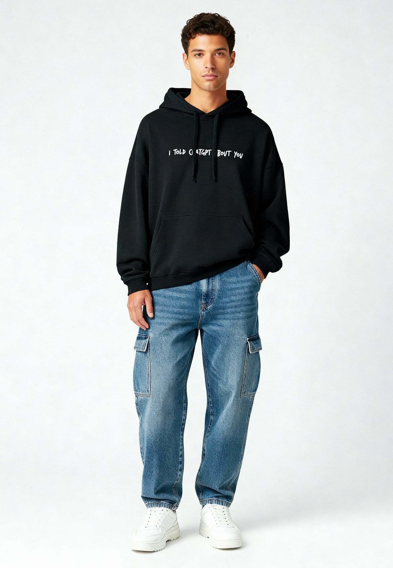Felpa nera con cappuccio e testo bianco, abbinata a jeans cargo azzurri chiari e sneaker bianche. Stile casual con una vestibilit�à rilassata.