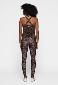 Top sin mangas de estampado de leopardo marrón con tirantes cruzados, acompañado de leggings a juego. Ambos hechos de tejido elástico, ajustándose al cuerpo.