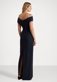 Váll nélküli, tengerészkék estélyi ruha, pliszírozott nyakkivágással, testhez álló szabással és térdtől szegélig húzódó oldalsó hasítékkal. Sima anyagszerkezet.