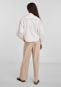 Hvit bomullsskjorte med puffede ermer og blonder, kombinert med beige vidde linbukser. Outfiten har en avslappet passform og naturlige teksturer.