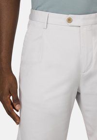 Un pantalon gris clair présente une texture lisse, un devant plat, des poches latérales et une fermeture à bouton avec un bouton marron clair contrastant.