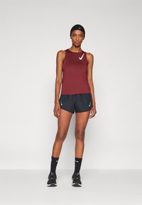 Haut sans manches bordeaux, shorts noirs, bandeau noir et baskets noires avec des accents blancs. Tissu lisse avec une coupe athlétique.