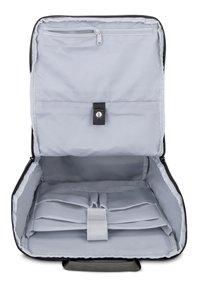 Intérieur d'un sac à dos en tissu gris avec une poche zippée, une fermeture à pression et des compartiments élastiques pour l'organisation. Texture textile lisse.