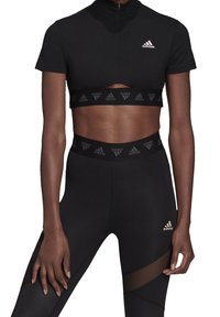 Černý sportovní crop top se zipovým límcem a výřezovým designem. Černé legíny s texturovaným pasem a průhlednými panely po stranách.