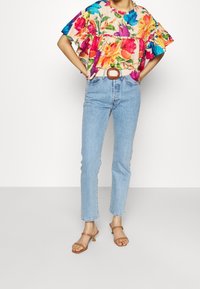 Blomstermønstret kortærmet top med flæser på ærmerne, parret med lysblå jeans og brune hæle-sandaler med ankellukning.